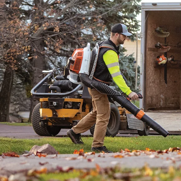 Landscape professional running commercial power equipment beside a zero-turn mower